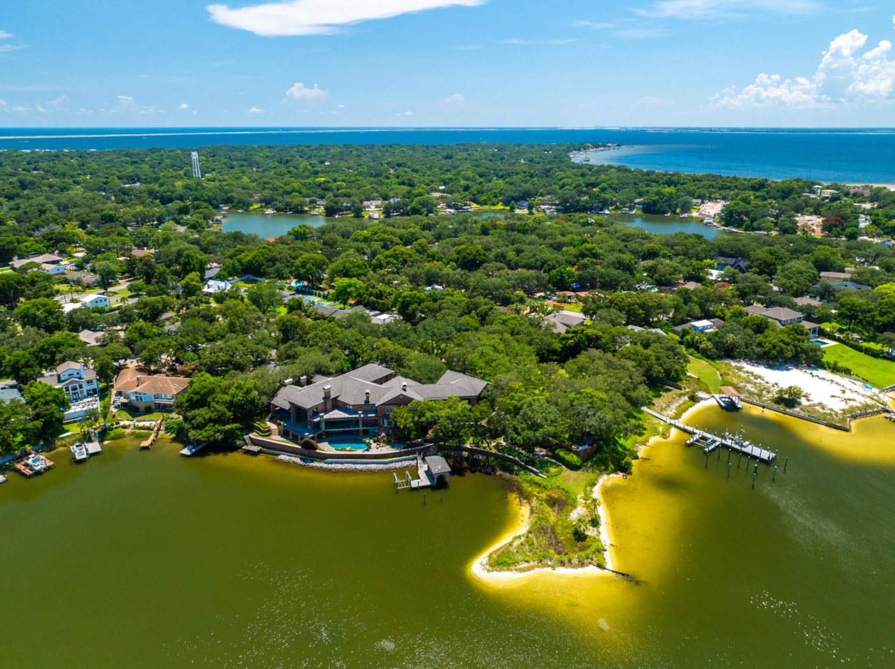 Aerial view of 204 Laura Lane, a three-story brick bayfront estate on Pensacola Bay with 675 feet of shoreline, a private cove, and a deep-water dock surrounded by emerald water